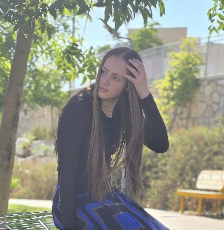 בעלת האתר MARTIN עם שיער ארוך, חולצה שחורה וחצאית כחולה ושחורה, ויד מורמת לצד הפנים